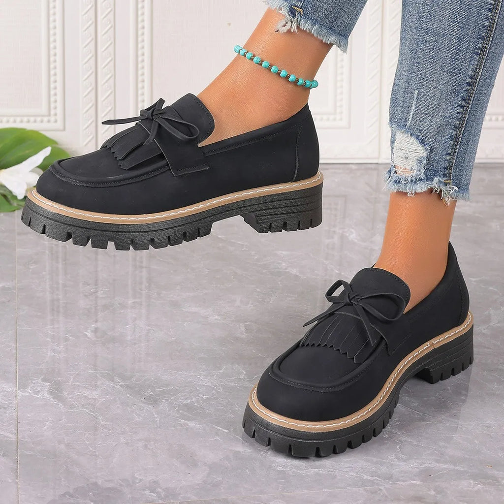 Black plus size women's loafers with a tassel and bowknot on a chunky rubber sole.