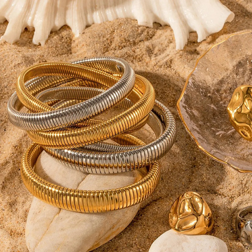 Gold titanium steel women's bracelet with elastic band and exaggerated vertical stripe ring pattern.