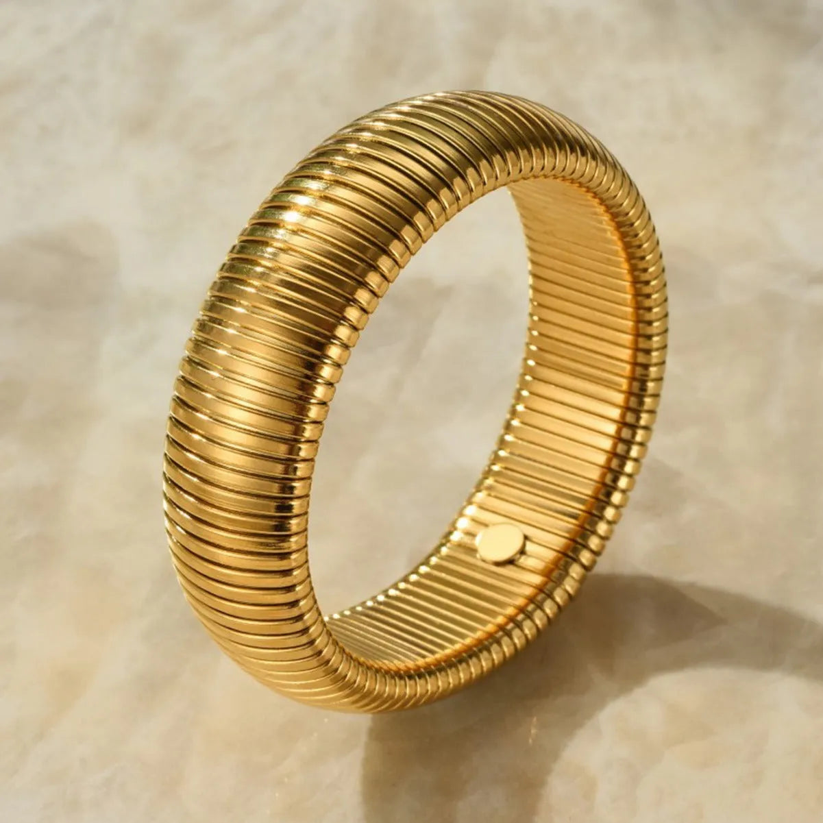 Gold titanium steel women's bracelet with elastic band and exaggerated vertical stripe ring pattern.