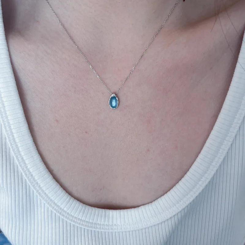 Navy blue water droplet necklace with geometric cross chain on white background