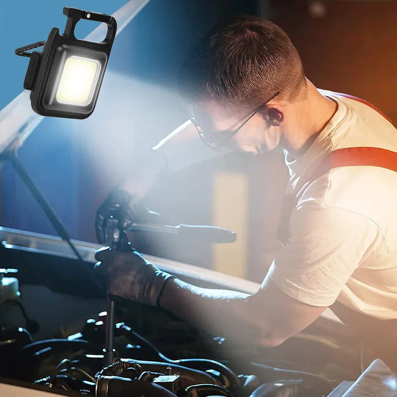 Black aluminium alloy COB keychain flashlight on a metal surface, magnetic base attached, 6x4.2cm size, with foldable handle extended