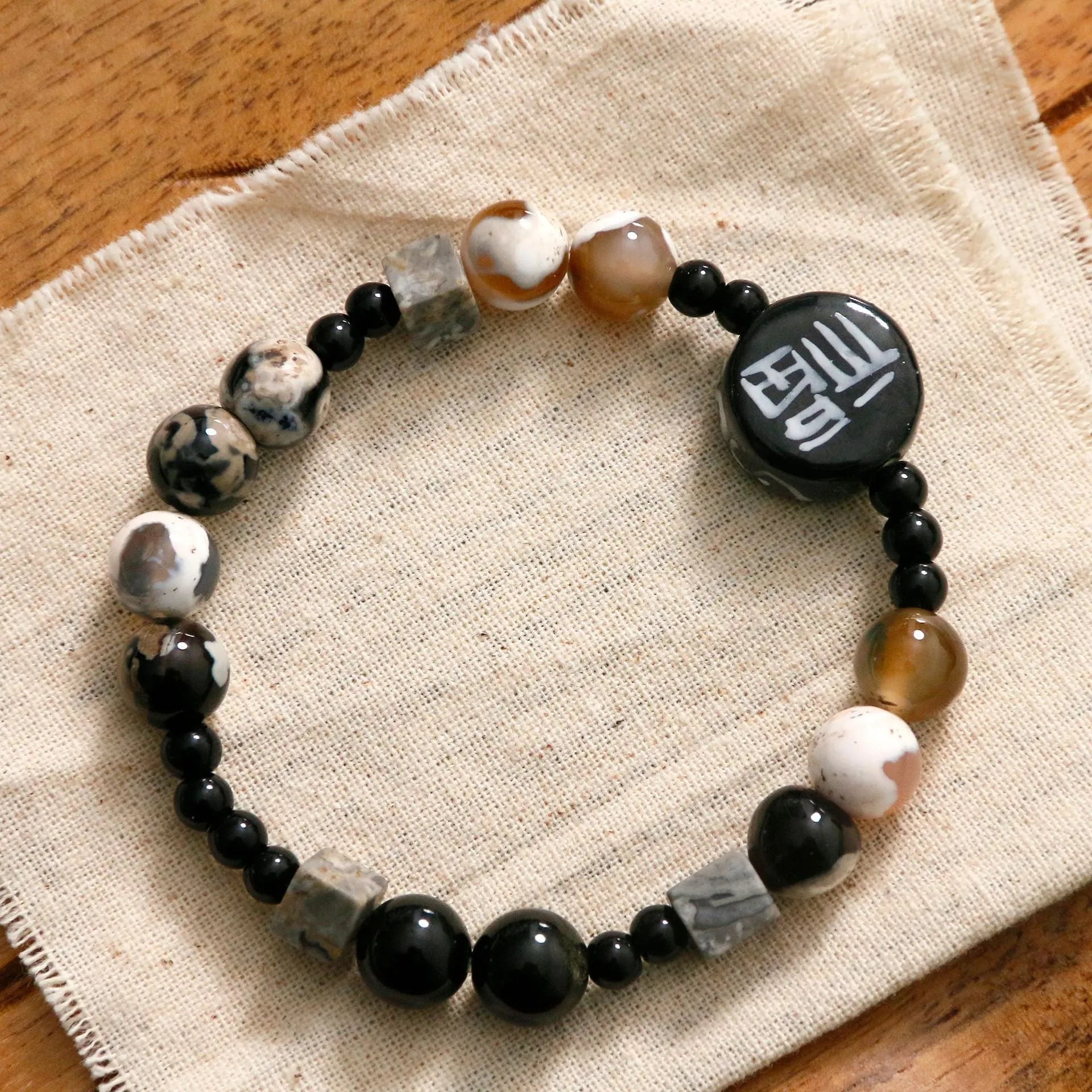 Hand-woven natural glitter stone black agate ceramic bracelet with round geometric beads on a neutral background