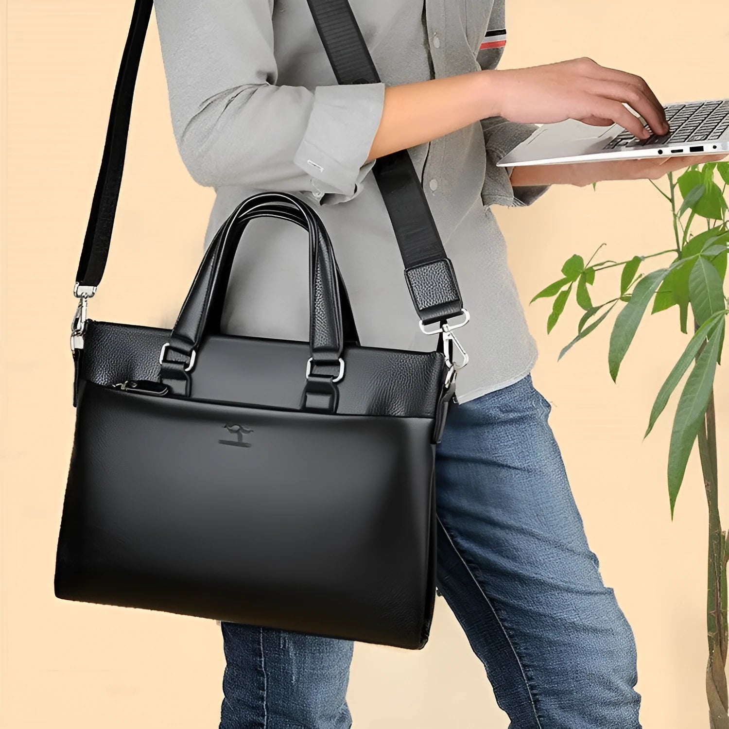 Men's black PU leather crossbody messenger bag with splicing design, shown next to a tablet for scale.