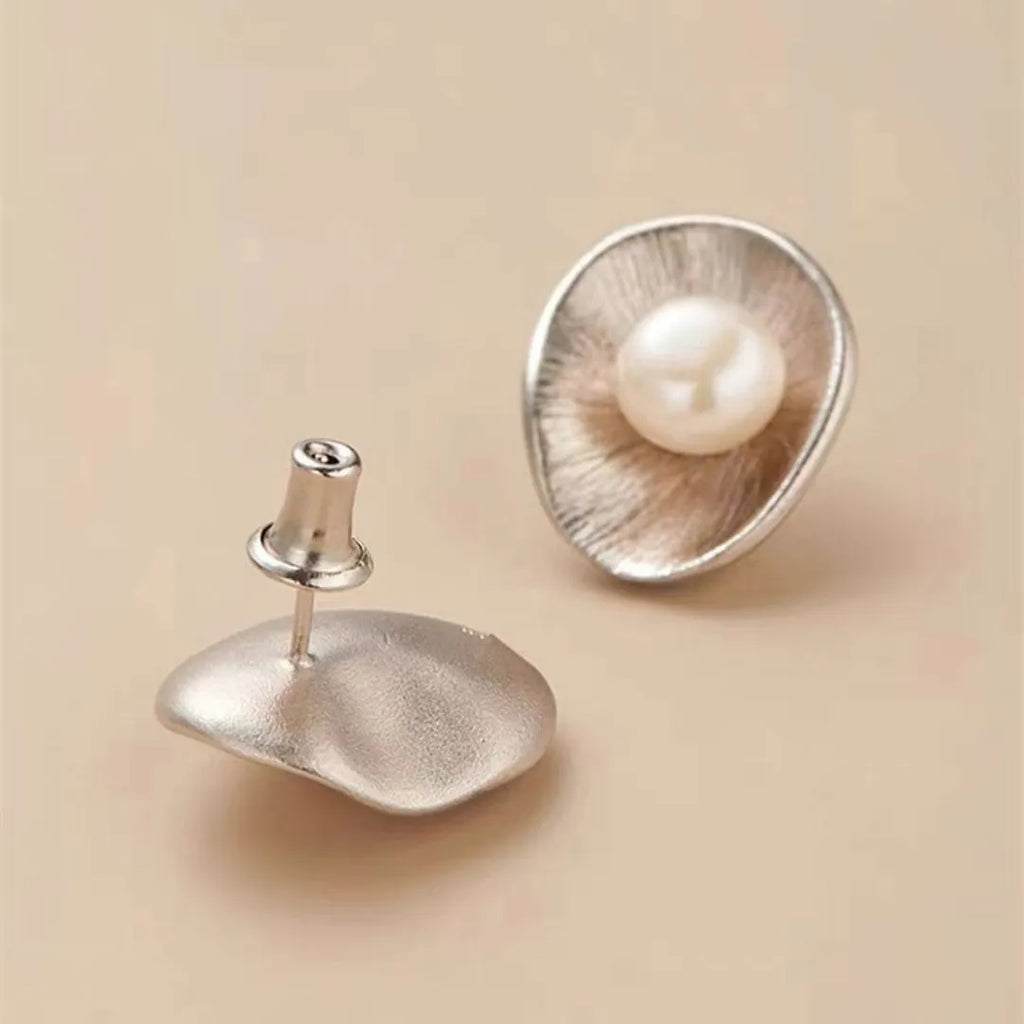 A pair of silver geometric stud earrings with white pearl details on a white background.