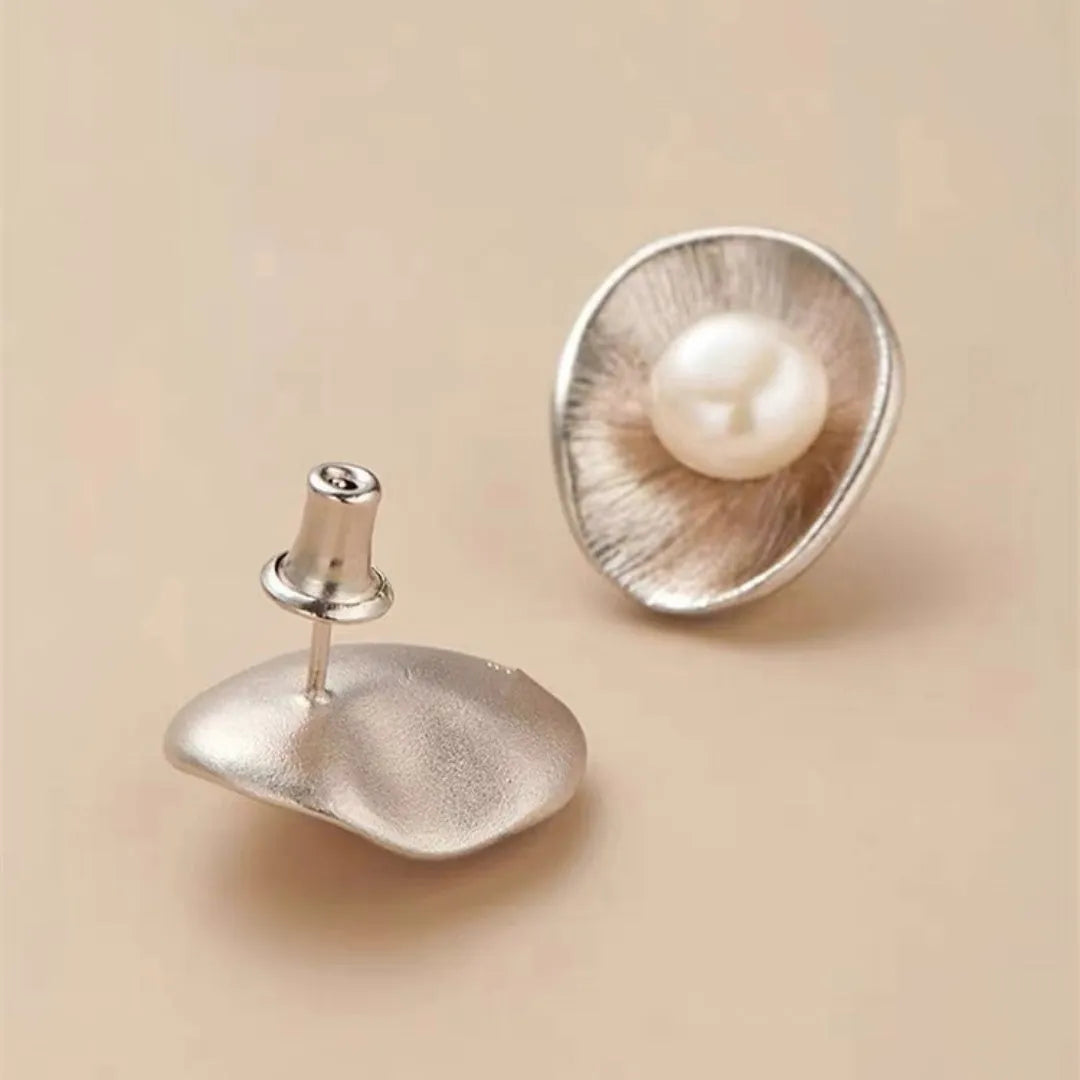 A pair of silver geometric stud earrings with white pearl details on a white background.