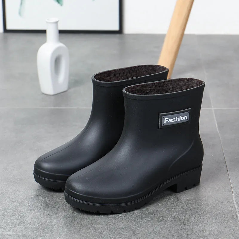 Women's black PVC mid-calf rain boot with a low heel on a wet surface.