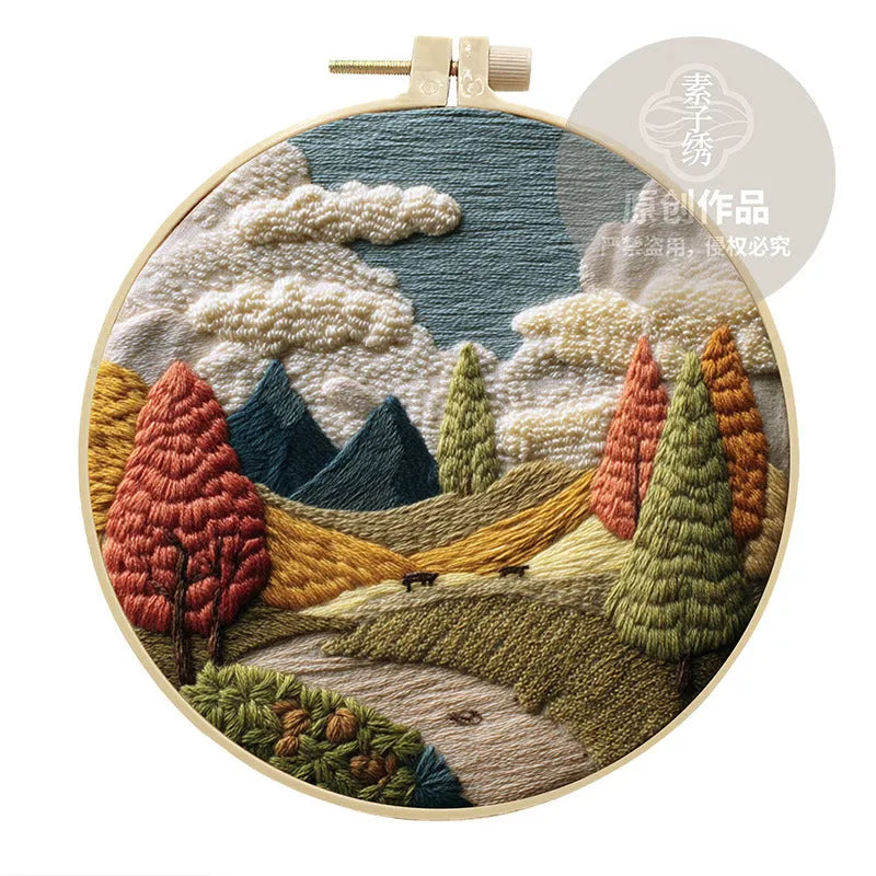 Embroidery DIY kit with cotton landscape fabric, bamboo frame, threads, and tools on wooden surface