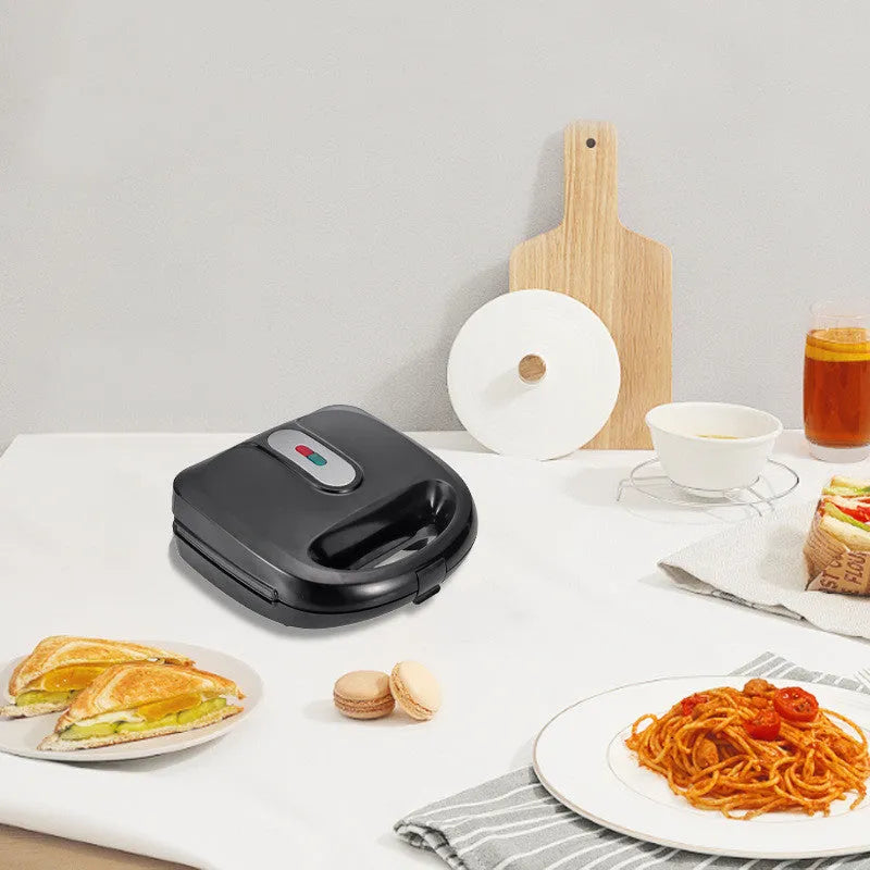 Black double-sided electric sandwich pan with brushed stainless steel cover on a kitchen counter.