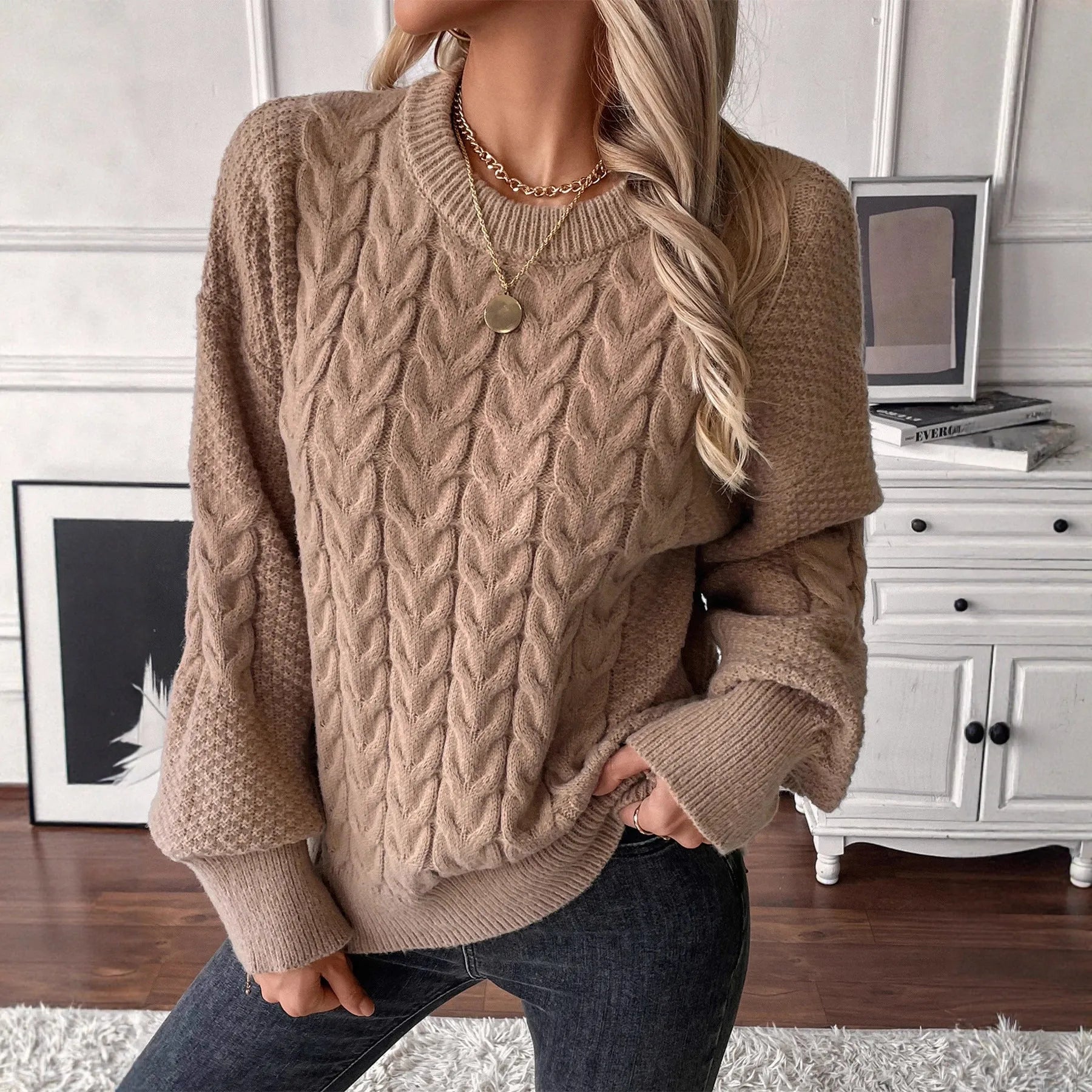 Woman wearing a loose beige round neck sweater with a twisted knit texture detail on the front.