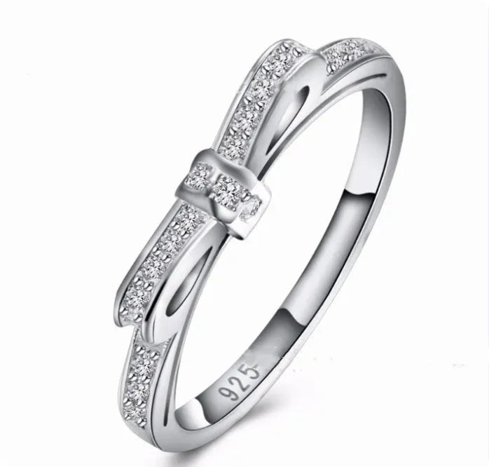 Silver bow-shaped crystal ring with zircon rhinestones on a finger.
