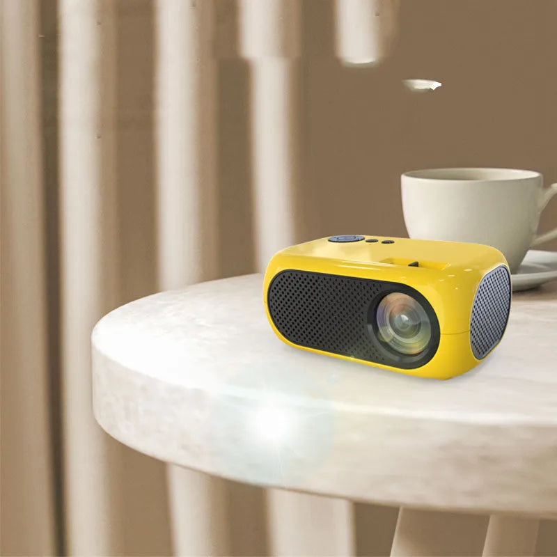 Compact gold and white M24 micro mini LED projector on a table with power adapter and AV cable.