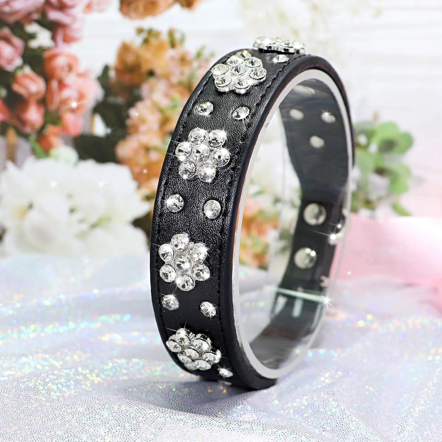 Close-up of a black PU leather dog collar with a studded rhinestone flower pattern and a metal D-ring.