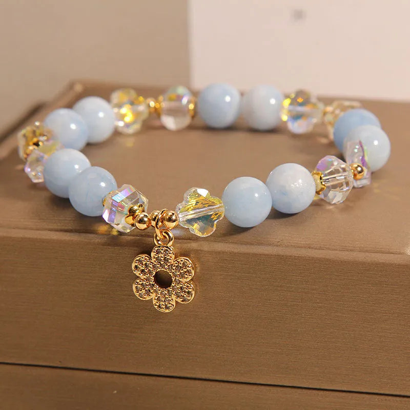 Women's aquamarine crystal bracelet with four-leaf clover design and pearl accents on a wrist.