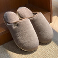 Solid colour winter plush slippers with non-slip PVC sole on a wooden floor.
