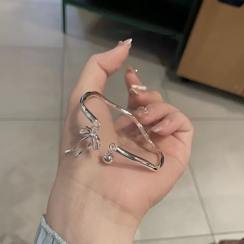 Silver adjustable bracelet with bow charm and small bell detail on wrist