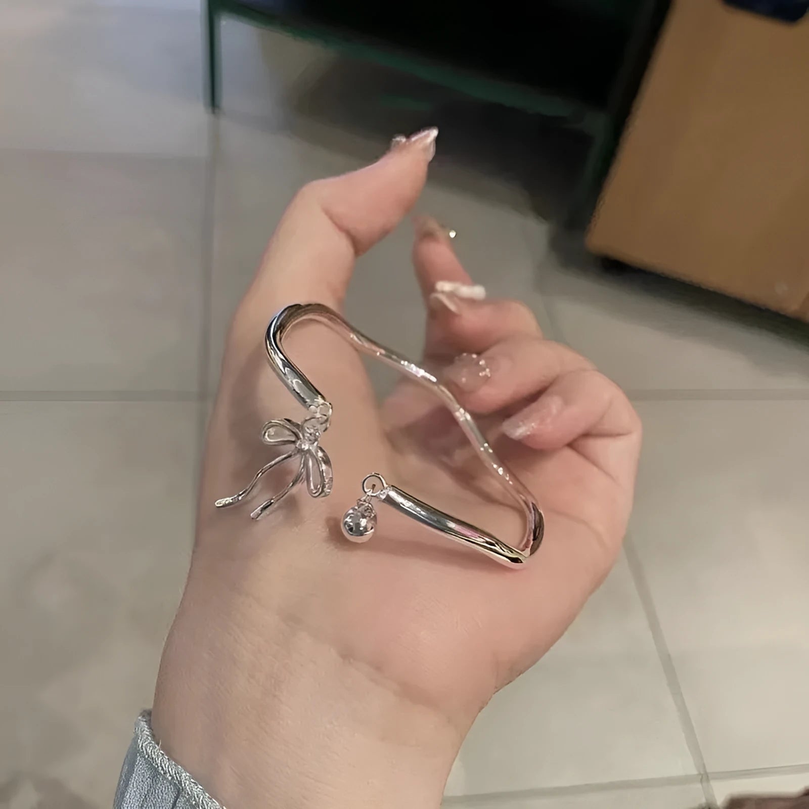Silver adjustable bracelet with bow charm and small bell detail on wrist