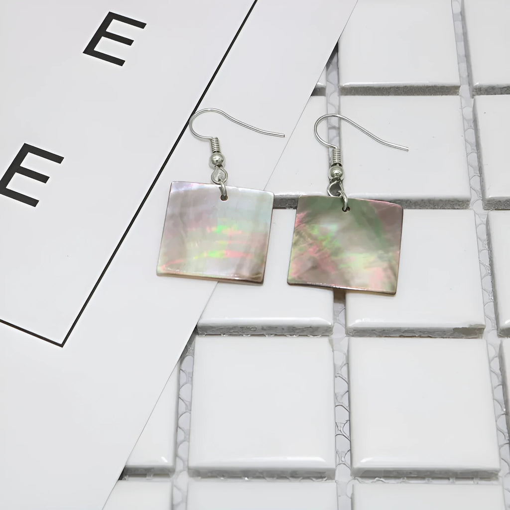 A pair of geometric-shaped shell stud earrings on a plain background, showing the natural texture.