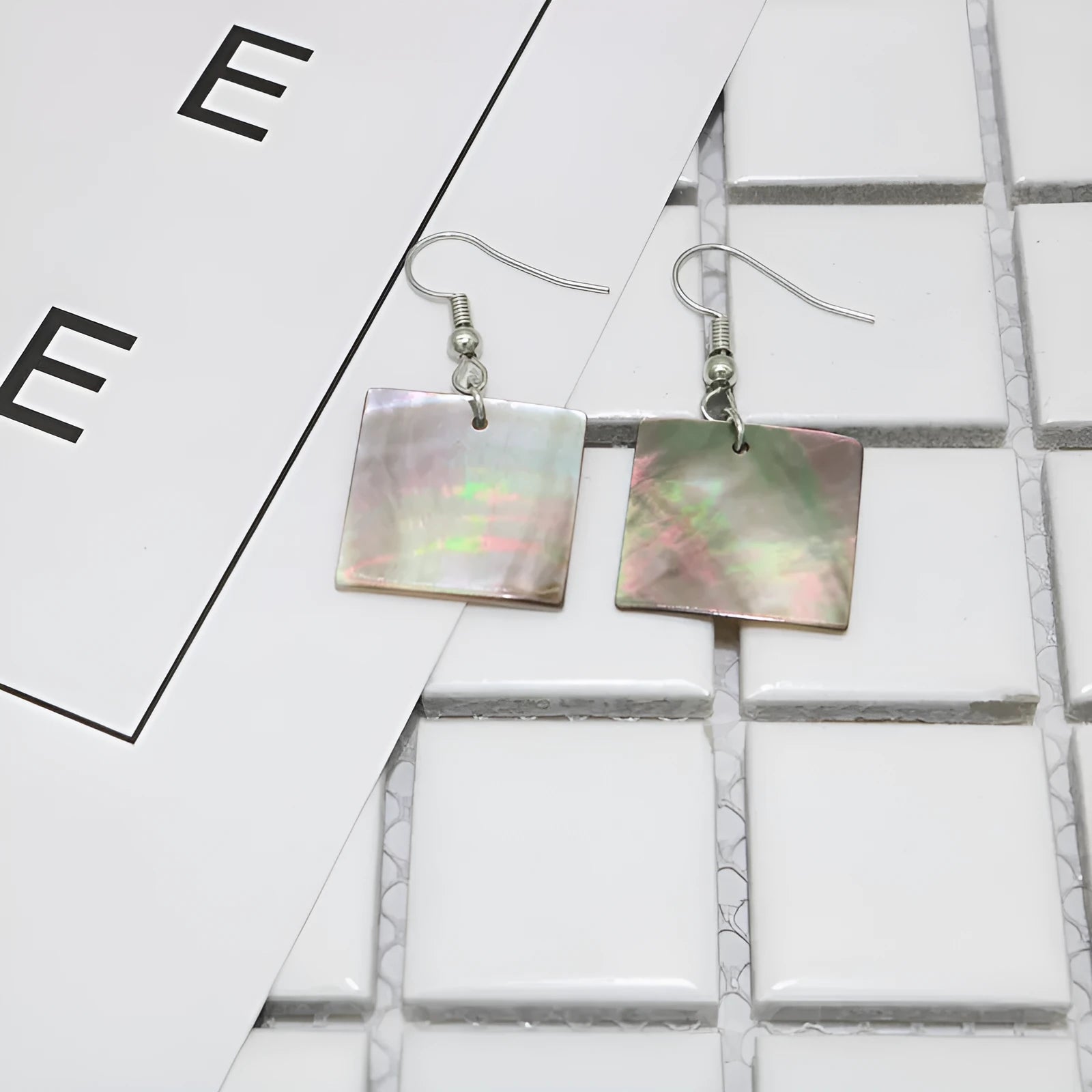 A pair of geometric-shaped shell stud earrings on a plain background, showing the natural texture.