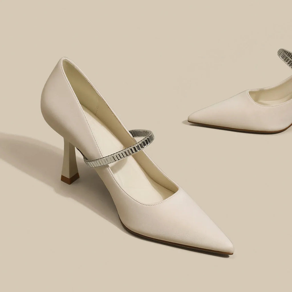 Women's black stiletto heel sandals with pointed closed toe, buckle strap, and skirt detail on a white background