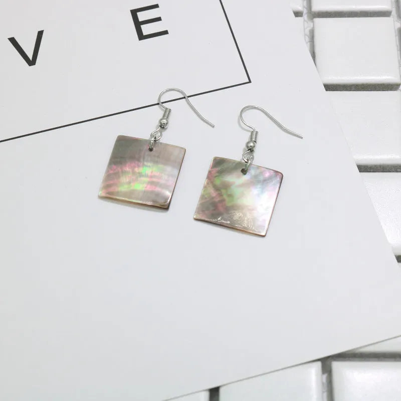 A pair of geometric-shaped shell stud earrings on a plain background, showing the natural texture.