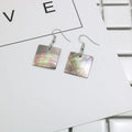A pair of geometric-shaped shell stud earrings on a plain background, showing the natural texture.
