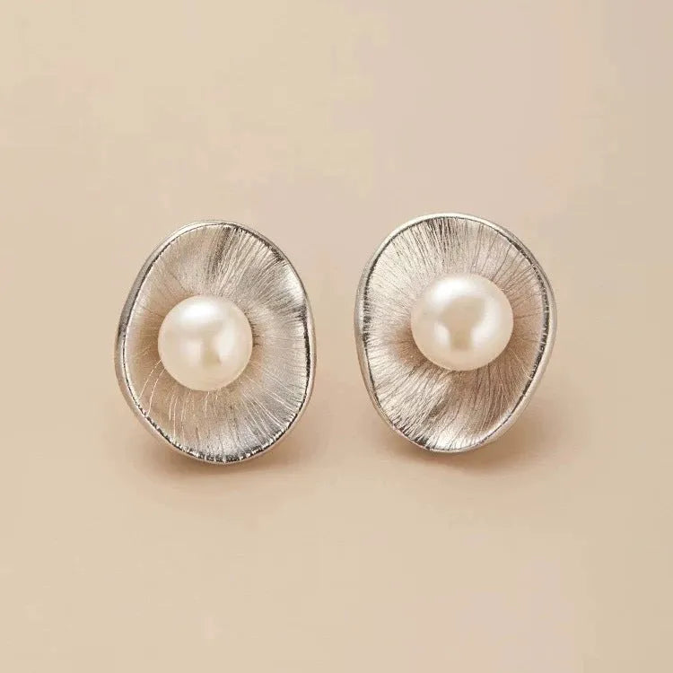 A pair of silver geometric stud earrings with white pearl details on a white background.