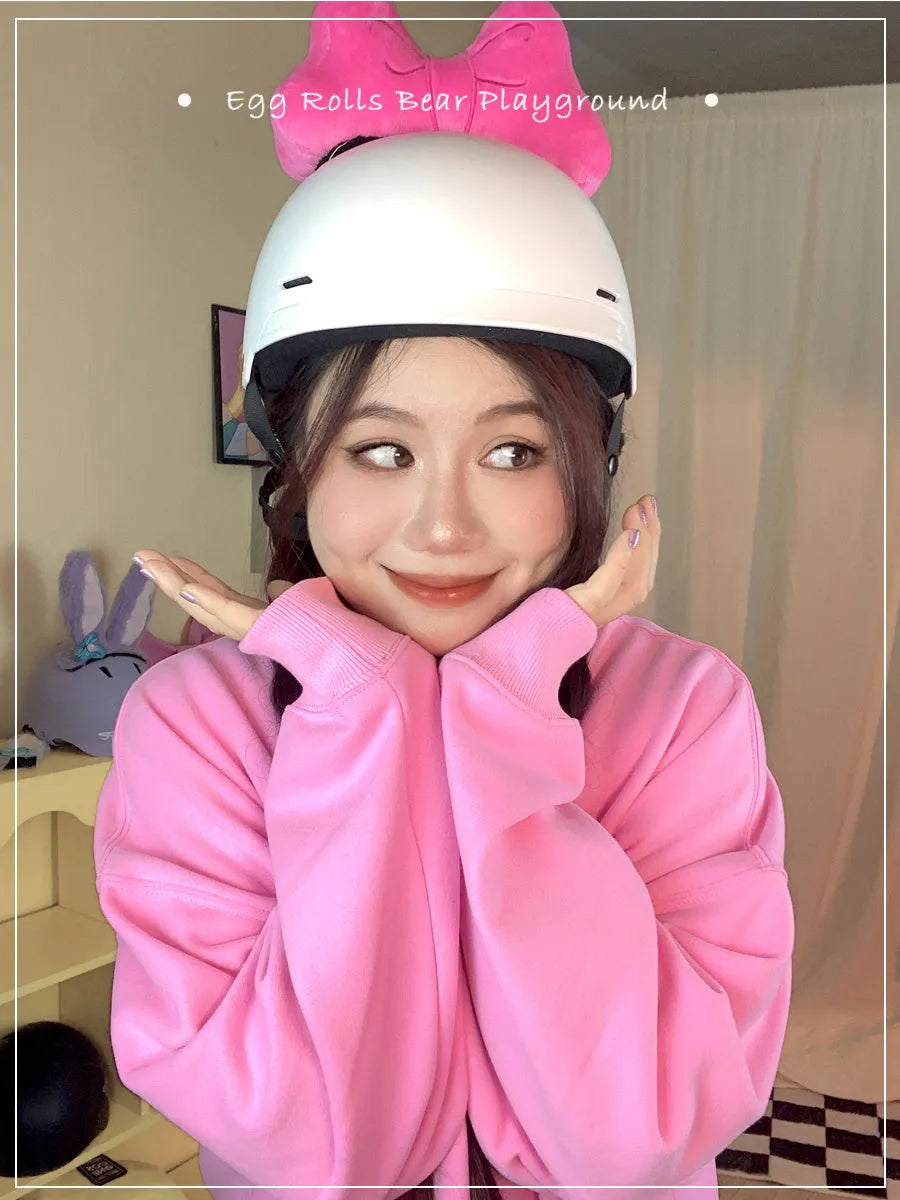 Plush bow tie helmet decoration in red, peach pink, and rose pink colours shown on a motorcycle helmet.