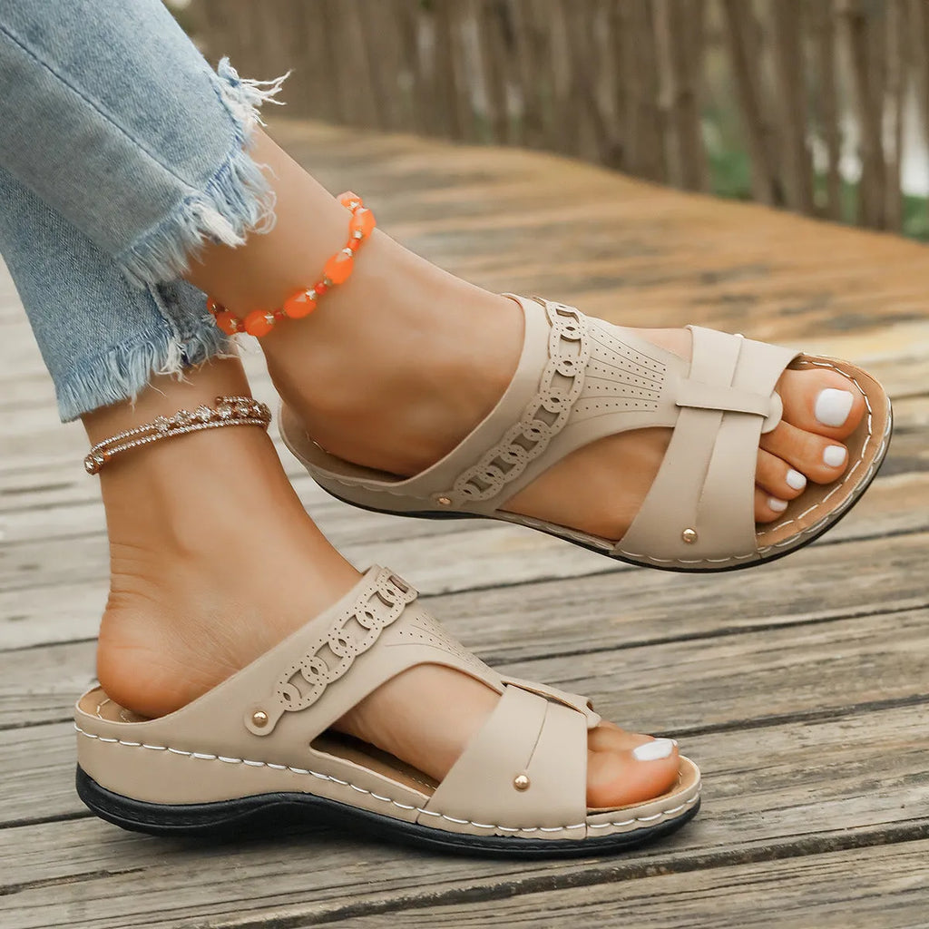 Pair of beige Roman style slippers with a fish mouth toe and slope heel on a rubber sole.