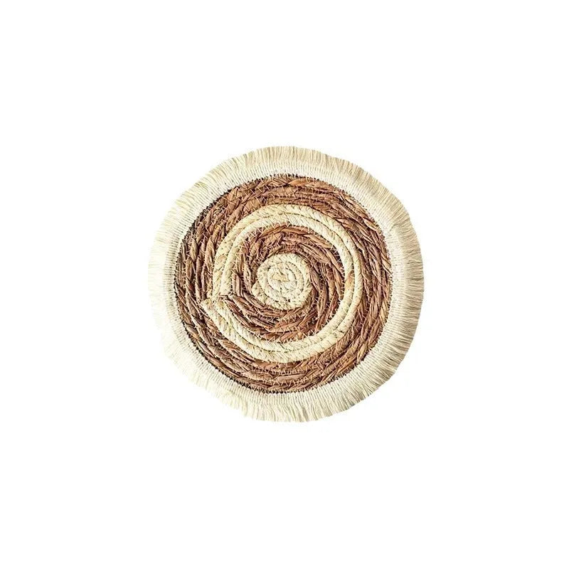 A round natural papyrus placemat with decorative tassels, shown on a wooden table.