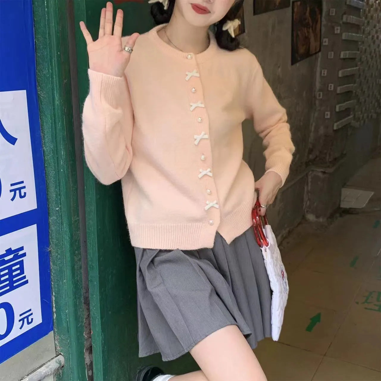 Women's light blue cardigan sweater with a black bow and pearl buttons, open over a white top.