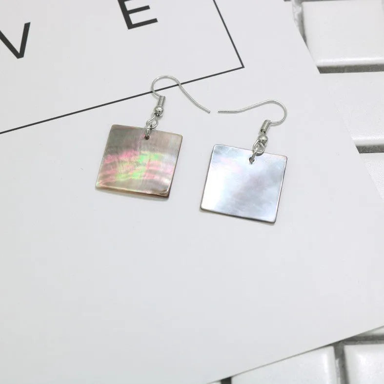 A pair of geometric-shaped shell stud earrings on a plain background, showing the natural texture.