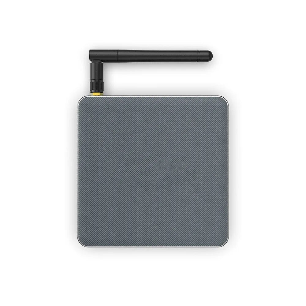 Square black Android TV set-top box with HDMI port and remote control on a wooden surface
