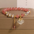 Women's natural strawberry quartz and white agate crystal bracelet with auspicious cloud pattern on a flat surface