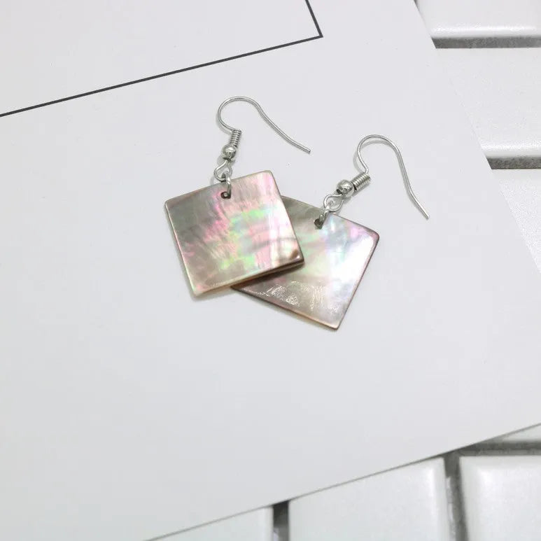 A pair of geometric-shaped shell stud earrings on a plain background, showing the natural texture.