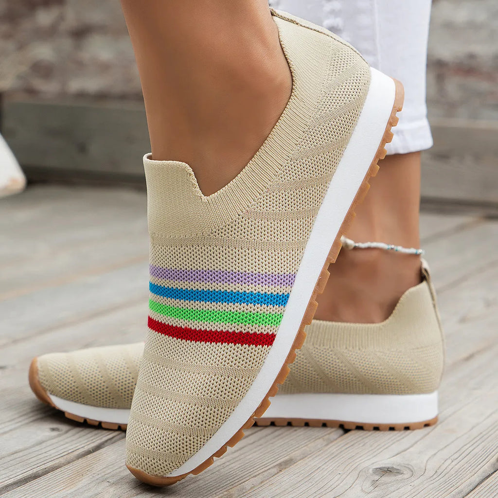 Women's casual flat sneaker pumps in beige with low wedge heel and round toe, side view on wooden floor