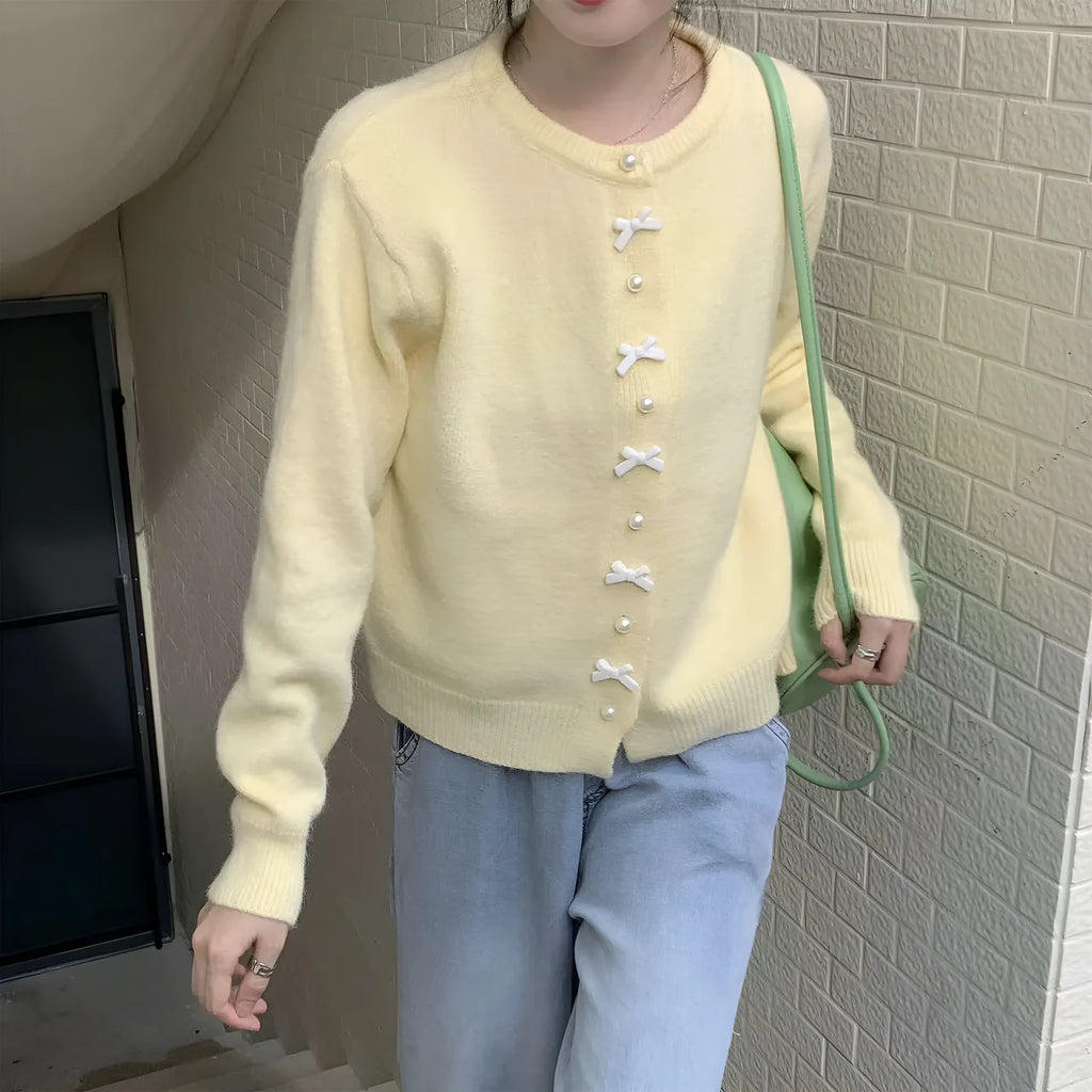 Women's light blue cardigan sweater with a black bow and pearl buttons, open over a white top.