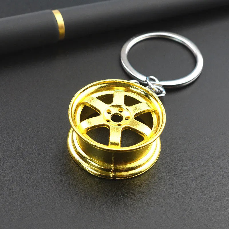 Zinc alloy car wheel hub keychain in gold finish with detailed hub pattern on white background