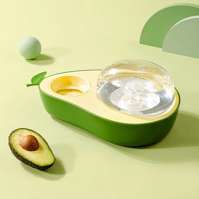 Avocado-shaped automatic water pet feeder with a green water reservoir and a pink slow food bowl on a white surface