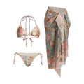 Creamy-white floral print women's three-piece bikini set with top, briefs, and skirt on a beach background.