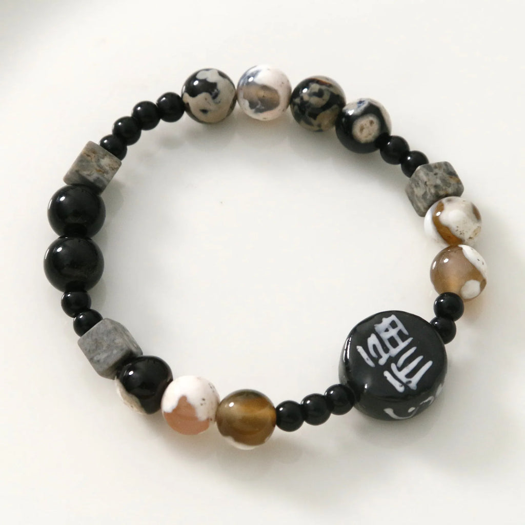 Hand-woven natural glitter stone black agate ceramic bracelet with round geometric beads on a neutral background
