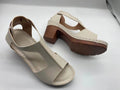 Women's beige peep toe wedge sandals with Roman ankle straps and a buckle closure on a low heel.