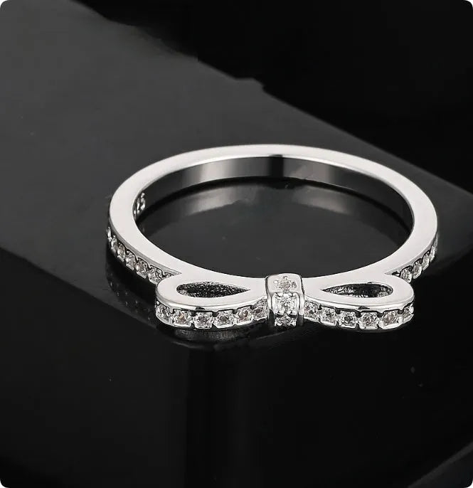 Silver bow-shaped crystal ring with zircon rhinestones on a finger.