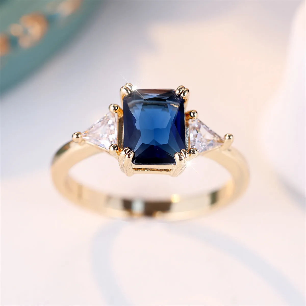 Gold sapphire blue rectangular copper ring for women on plain background