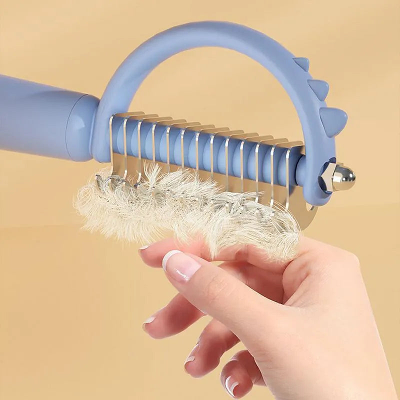 Blue dinosaur-shaped self-cleaning cat brush with stainless steel bristles on a white background