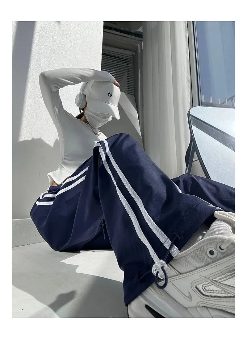 Navy blue loose straight-leg trousers with ribbon parallel bars contrast detail on a hanger.