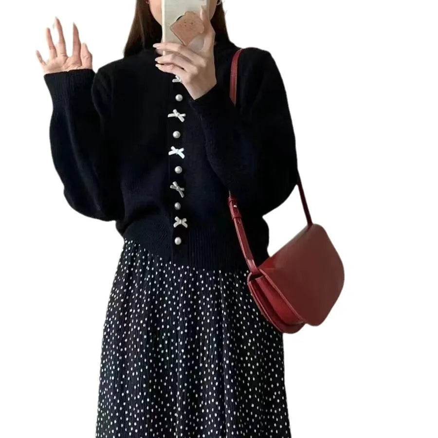 Women's light blue cardigan sweater with a black bow and pearl buttons, open over a white top.