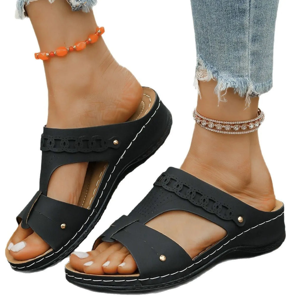 Pair of beige Roman style slippers with a fish mouth toe and slope heel on a rubber sole.