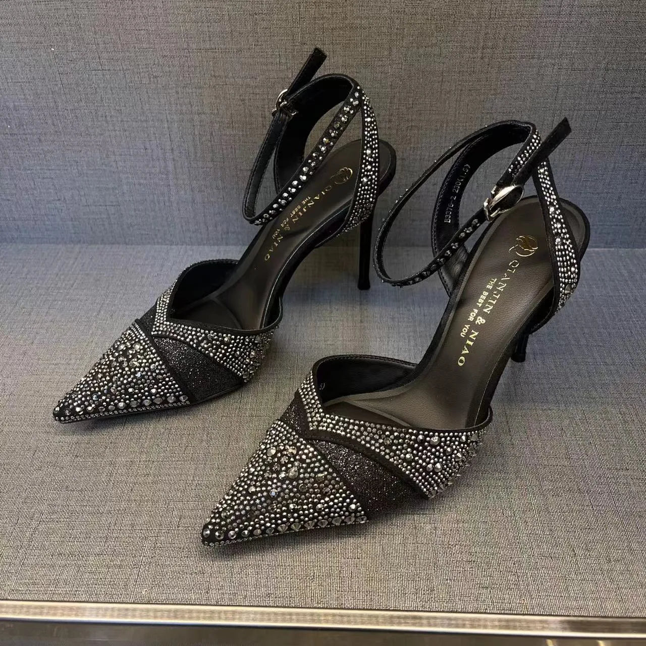 Women's black high heel shoe with pointed toe, stiletto heel, red sole, and hollow design detail.