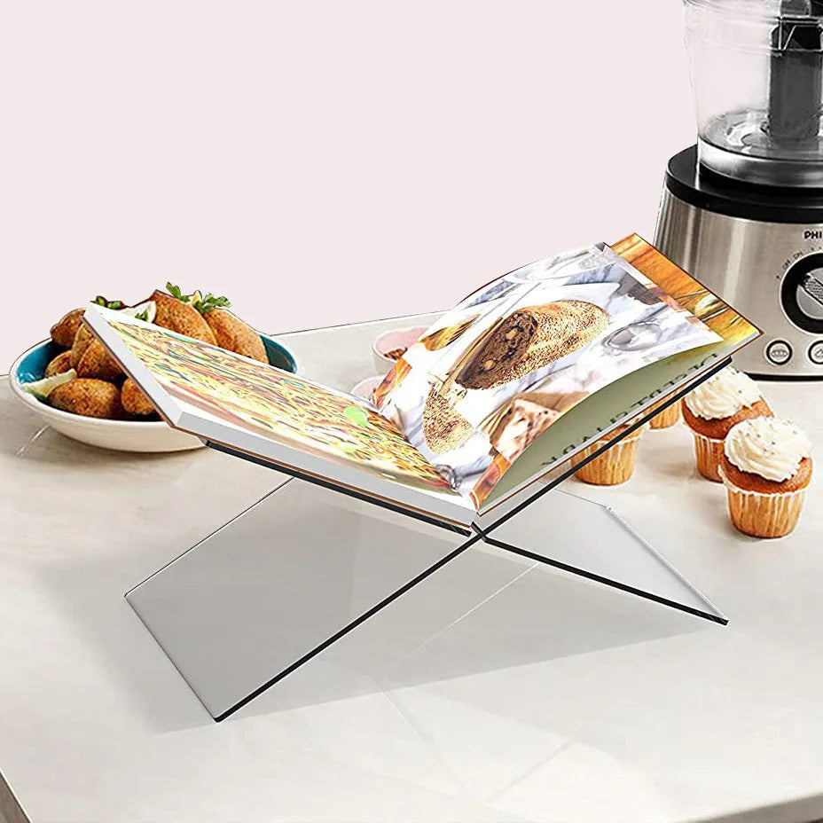 Clear acrylic X-shaped book reading rack displaying hardback books on a wooden desk