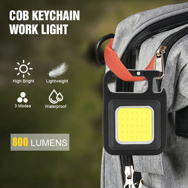Black aluminium alloy COB keychain flashlight on a metal surface, magnetic base attached, 6x4.2cm size, with foldable handle extended